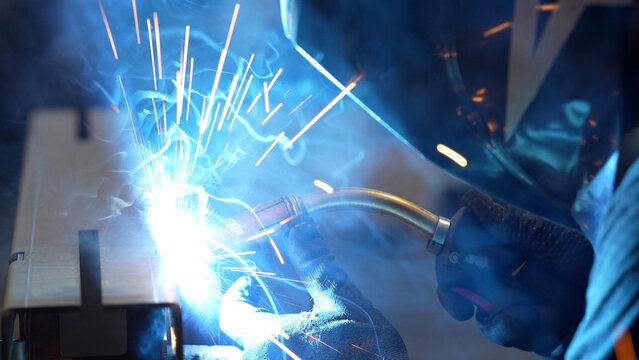 Striking close-up of bright sparks flying from heavy industrial equipment during a metalworking process. The image captures the intense heat and dynamic energy of modern manufacturing