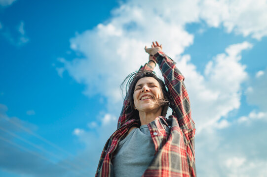Smiling woman raises her arms towards the cloudy sky in a field