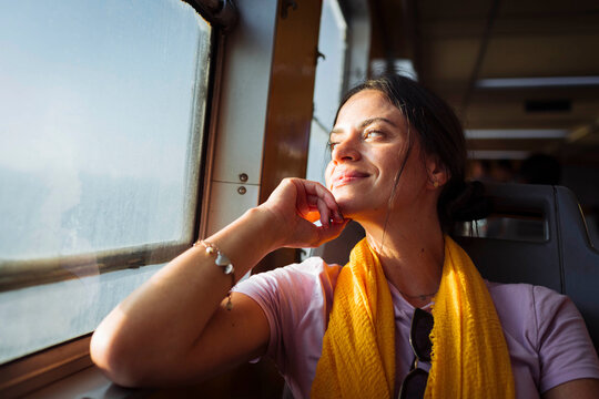 Smiling woman with hand on chin looking through train window