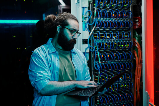 IT expert working on laptop near server in control room