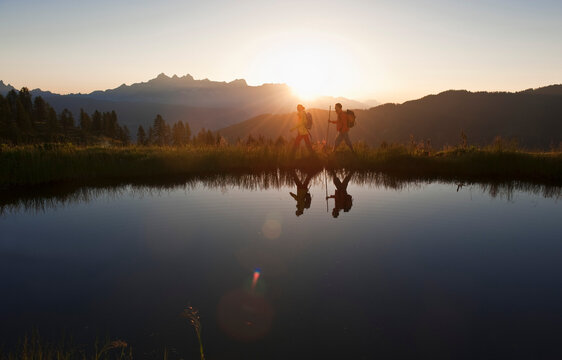 Man and woman hike near a mountain lake at sunrise in Austria