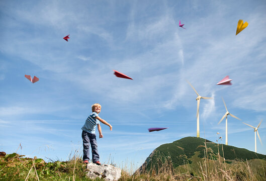 A boy throws a paper airplane near a wind turbine in Germany