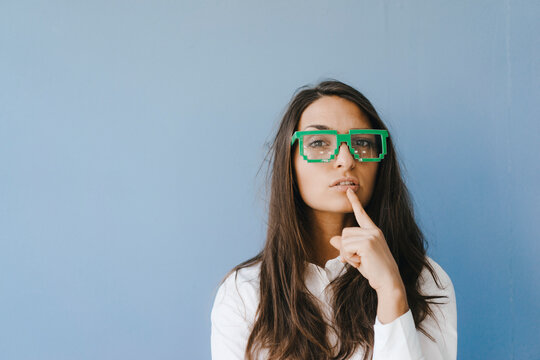 Young woman wearing pixel glasses, putting finger on mouth