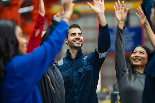 Industrial workers celebrating successful production with team high five inside manufacturing. Engineering professionals showing motivation, workplace success, employee engagement, factory teamwork.