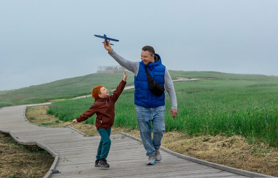 Father and son play with a toy airplane on a park boardwalk