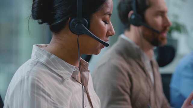 Close up concentrated multiethnic team operators in call center talking with headsets. Serious multiracial callcenter business agents two diversity men and Arabian saleswoman talk to customers advice