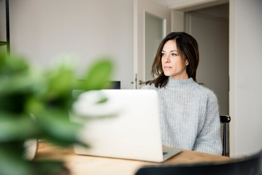 Woman sitting at table, using laptop, thinking