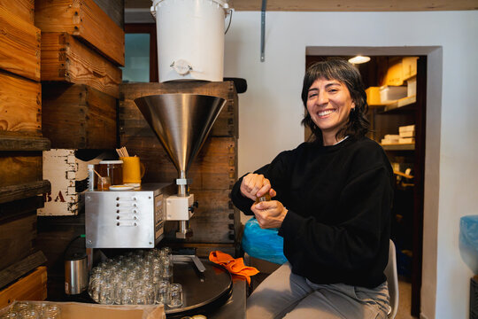 Smiling female beekeeper is bottling honey into jars in a workshop