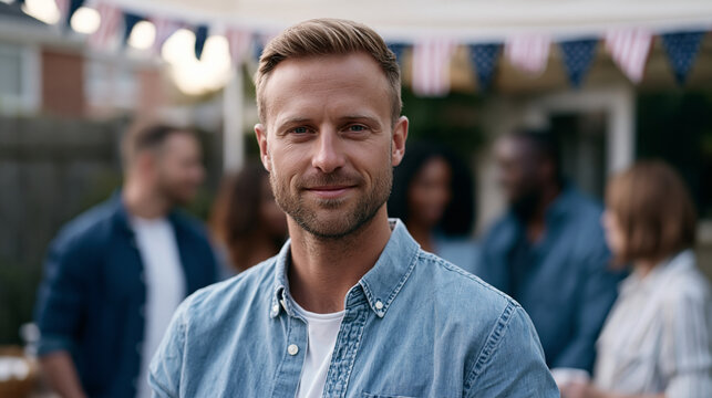 A trans man in his thirties stands with a group of coworkers at a summer company barbecue, slightly apart but visibly present, Fourth of July bunting overhead, perfect for gender