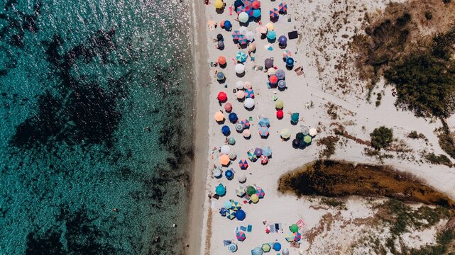 Aerial view shows colorful umbrellas on a sandy beach in Sardinia