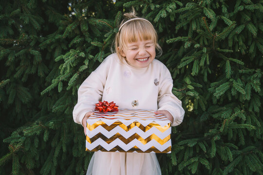 Excited girl holding gift box in front of fir tree