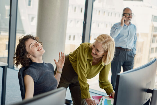 Colleagues laugh at an office desk while a man talks on the phone