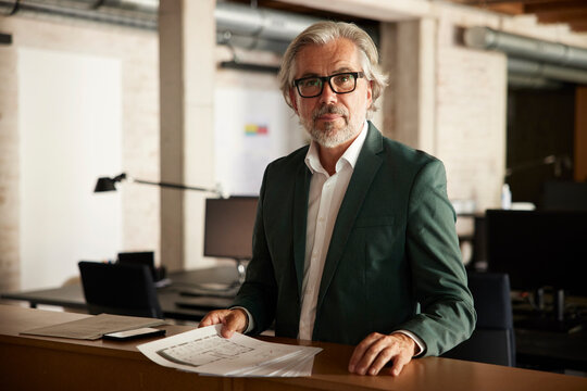 Male professional with documents standing at table in office
