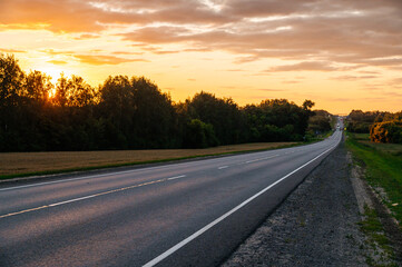 Fototapeta premium an empty highway in a field during a colorful pink sunset in the sky
