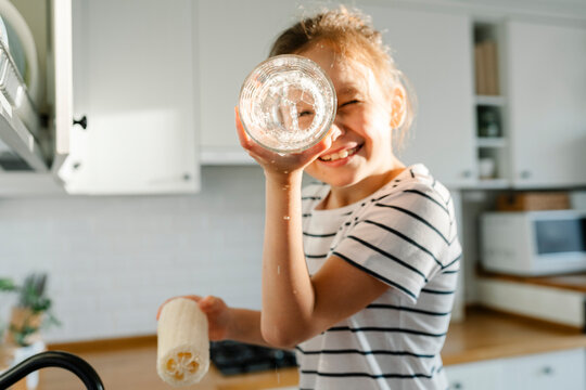 Playful girl washing dishes with loofah at home