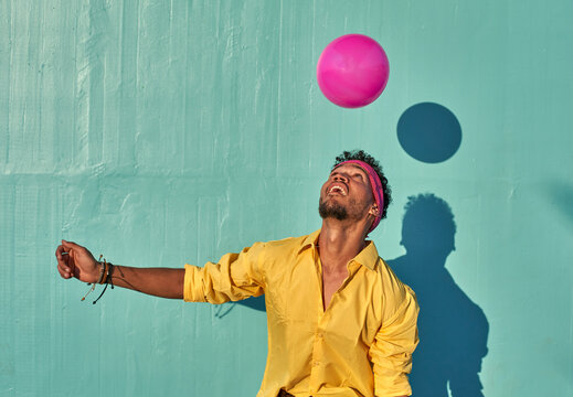 Young black man playing with a pink ball in front of a blue wall