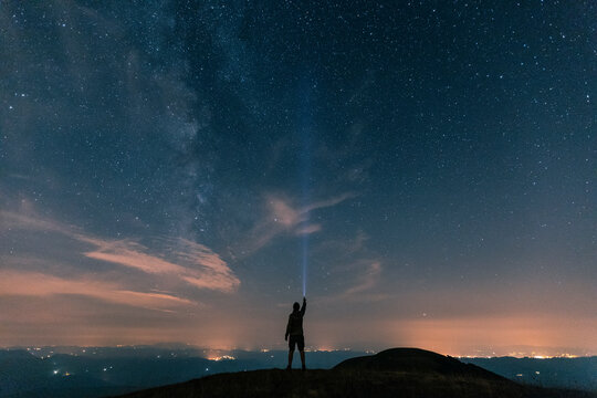 Italy, Monte Nerone, silhouette of a man with torch under night sky with stars and milky way