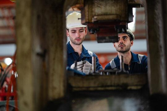 Industrial technicians inspecting heavy press machine during maintenance inside manufacturing factory. Engineering teamwork, equipment inspection, preventive maintenance, production quality.