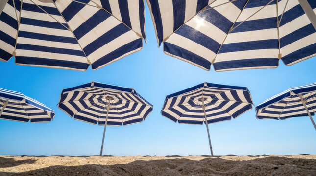 Blue and white striped parasols on sandy beach under clear blue sky on sunny day, creating relaxing summer atmosphere