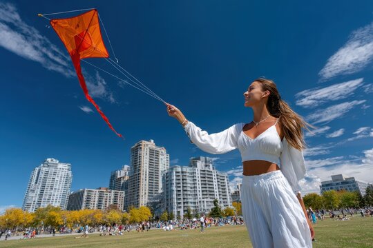 Woman enjoys flying a colorful kite on a sunny day in a city park with skyscrapers