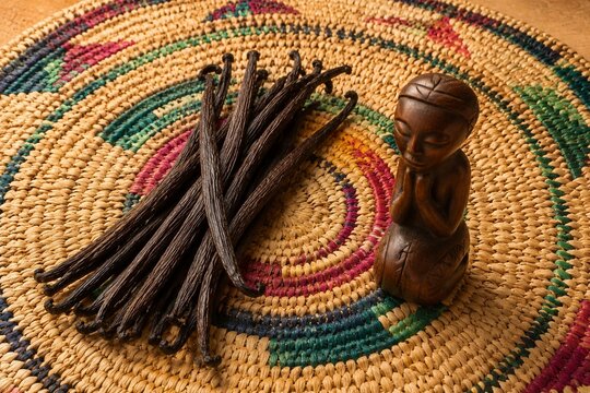 A handwoven raffia table mat with vanilla pods and a wooden carving.