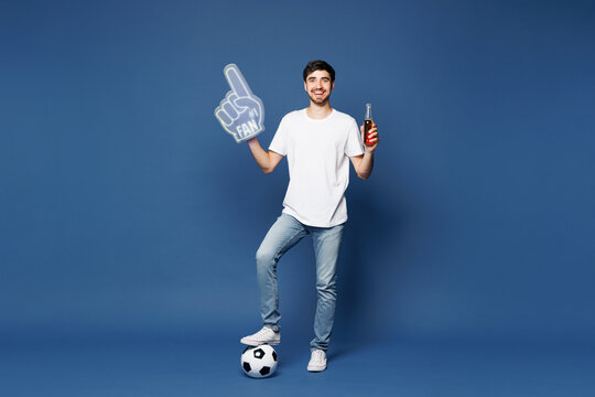 Full body young man fan wear white t-shirt foam 1 fan glove finger up drink beer cheer up support football sport team hold in hand soccer ball watch tv live stream isolated on plain blue background