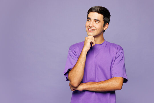 Young Caucasian man he wear violet t-shirt casual clothes put hand prop up on chin, lost in thought and conjectures isolated on plain pastel light purple background studio portrait. Lifestyle concept.