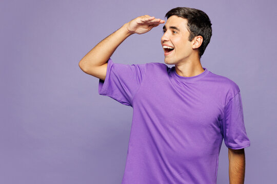 Young satisfied positive Caucasian man he wears violet t-shirt casual clothes hold hand at forehead look far away distance isolated on plain pastel light purple background studio. Lifestyle concept.
