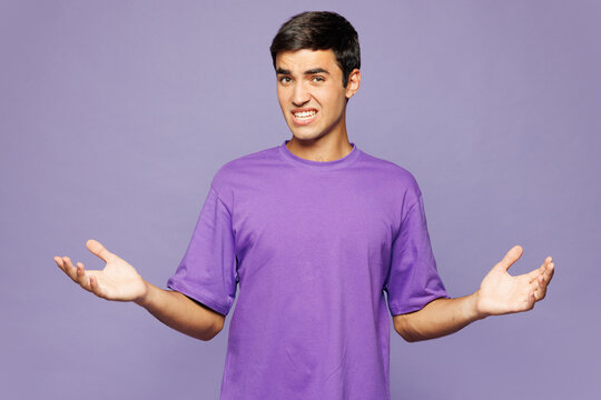 Young sad upset Caucasian man he wear violet t-shirt casual clothes shrugging shoulders looking puzzled spread hands isolated on plain pastel light purple background studio portrait. Lifestyle concept