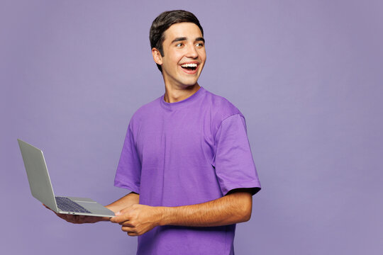 Young Caucasian IT man he wear violet t-shirt casual clothes hold use work on laptop pc computer look aside on area isolated on plain pastel light purple background studio portrait. Lifestyle concept.