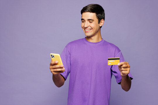 Young happy man he wears violet t-shirt casual clothes using mobile cell phone hold credit bank card doing online shopping order delivery booking tour isolated on plain pastel light purple background.