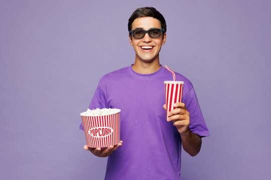 Young happy Caucasian man he wear violet t-shirt casual clothes 3d glasses watch movie film hold bucket of popcorn cup of soda pop in cinema isolated on pastel light purple background studio portrait.