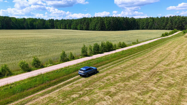 Silver SUV parked on dirt road alongside green wheat field under bright blue sky