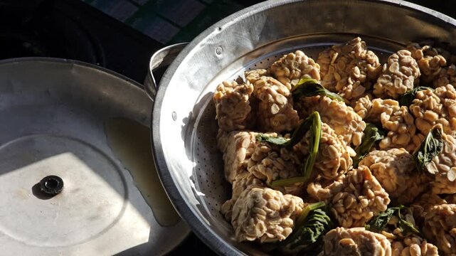 Close up view of fresh raw tempeh made from Glycine max in a metal steaming basket ready for cooking