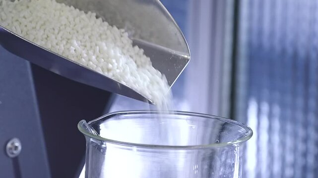 White plastic pellets poured into industrial processing equipment before polymer extrusion. Ideal for plastics manufacturing, engineering and production concepts.