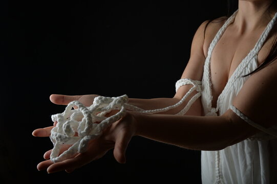 Junge Frau pr&auml;sentiert wei&szlig;es Baumwollseil in den H&auml;nden vor schwarzem Hintergrund. Ausdrucksstarkes Fine-Art-Motiv zu Vertrauen, Verbindung, Symbolik, Handwerk, Theater und Konzeptfotografie.