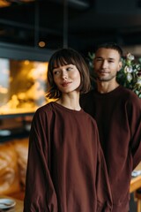 Fototapeta premium Stylish couple portrait in matching brown outfits for fashion banner and lifestyle background with warm cafe setting