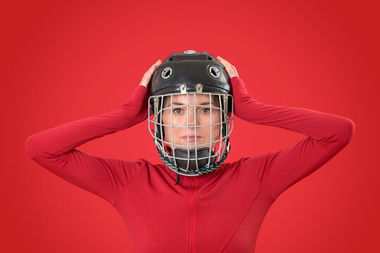 female hockey player in a cage helmet and red sportswear, hands on head