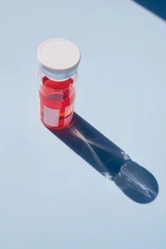 Clear glass vial with red solution for vaccine or drug development on blue background