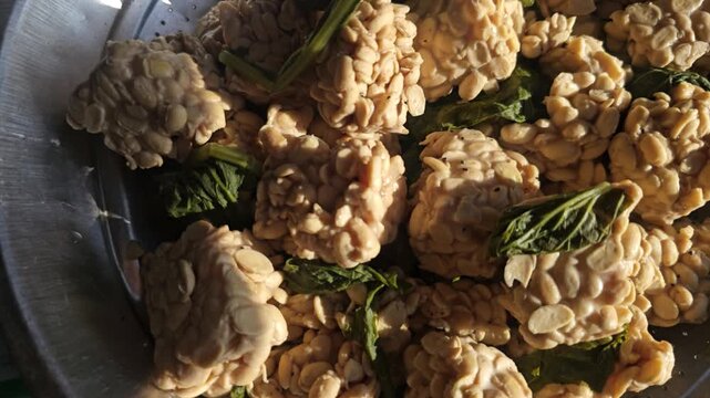 Close up pan of fresh raw tempeh blocks mixed with green herbs resting in a metal bowl