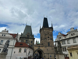 Obraz premium The Gothic Lesser Town Bridge Tower stands at the entrance to Charles Bridge in Prague. Historic architecture and a stone archway sit under a cloudy sky.
