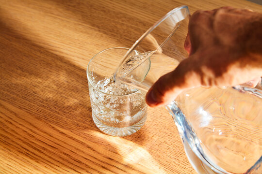 Pouring fresh clear water from a glass pitcher into a drinking glass on a wooden table
