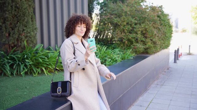 A young woman uses her smartphone outdoors in an urban area, reflecting modern communication