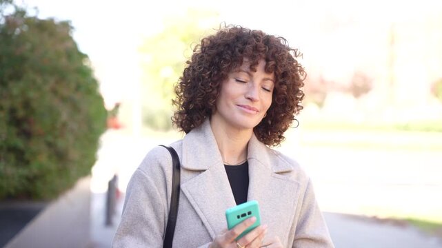 A Joyful Woman Happily Using Her Smartphone While Outdoors in Bright Natural Light