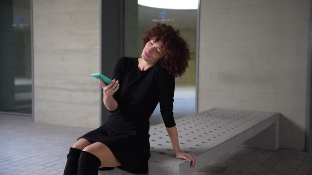 A Stylish Woman with Beautiful Curly Hair is Checking Her Phone in a Modern Interior Space