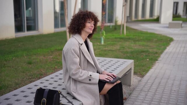 A Young Woman Engaged in Work on Her Laptop in an Urban Outdoor Setting, Enjoying Nature