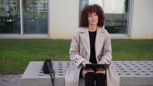 A modern professional is working outdoors in an urban setting while using a tablet