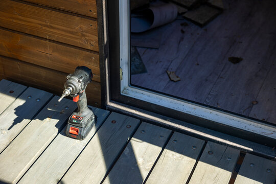 Cordless impact driver on wooden deck at private house entrance, sunny outdoor workspace. Concept: DIY home repair