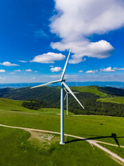 Obraz premium Wind turbine stands tall on green hills with blue sky and clouds during the day near wind farm in the countryside of the region