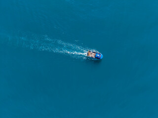 Naklejka premium Boat travels over clear blue water in a vast ocean, creating ripples as it moves under sunlight during a warm day in summer